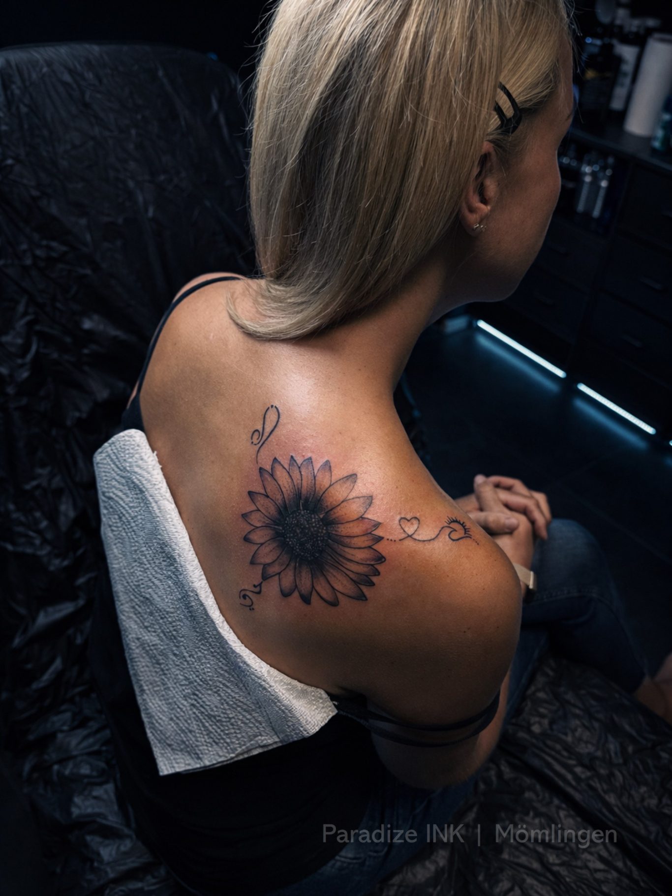Paradize INK Tattoo Mömlingen Eine Person mit blonden Haaren sitzt mit einem Sonnenblumen-Tattoo auf dem Rücken.