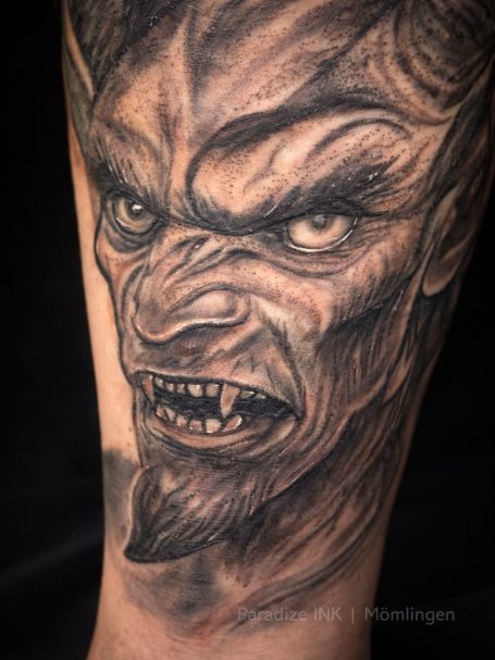 Detailliertes Tattoo eines grimmigen, dämonischen Gesichts mit scharfen Zähnen.