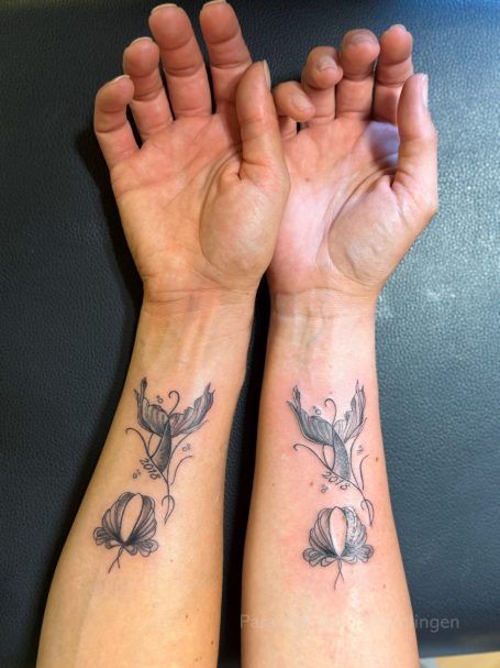 Tattoo von zwei Händen mit einem stilisierten Vogel und einer Blume auf den Unterarmen.