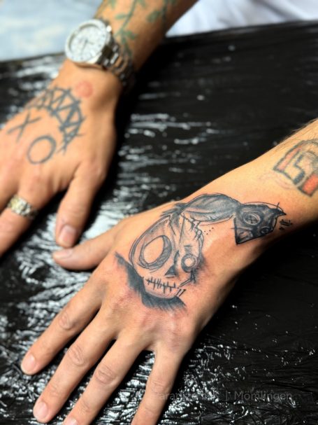 Nahaufnahme von tätowierten Händen mit verschiedenen Designs und einer Totenkopf-Tätowierung.