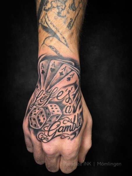 Tattoo auf Hand mit Motiven von Spielkarten und Würfeln, Schriftzug "Life's a Game".