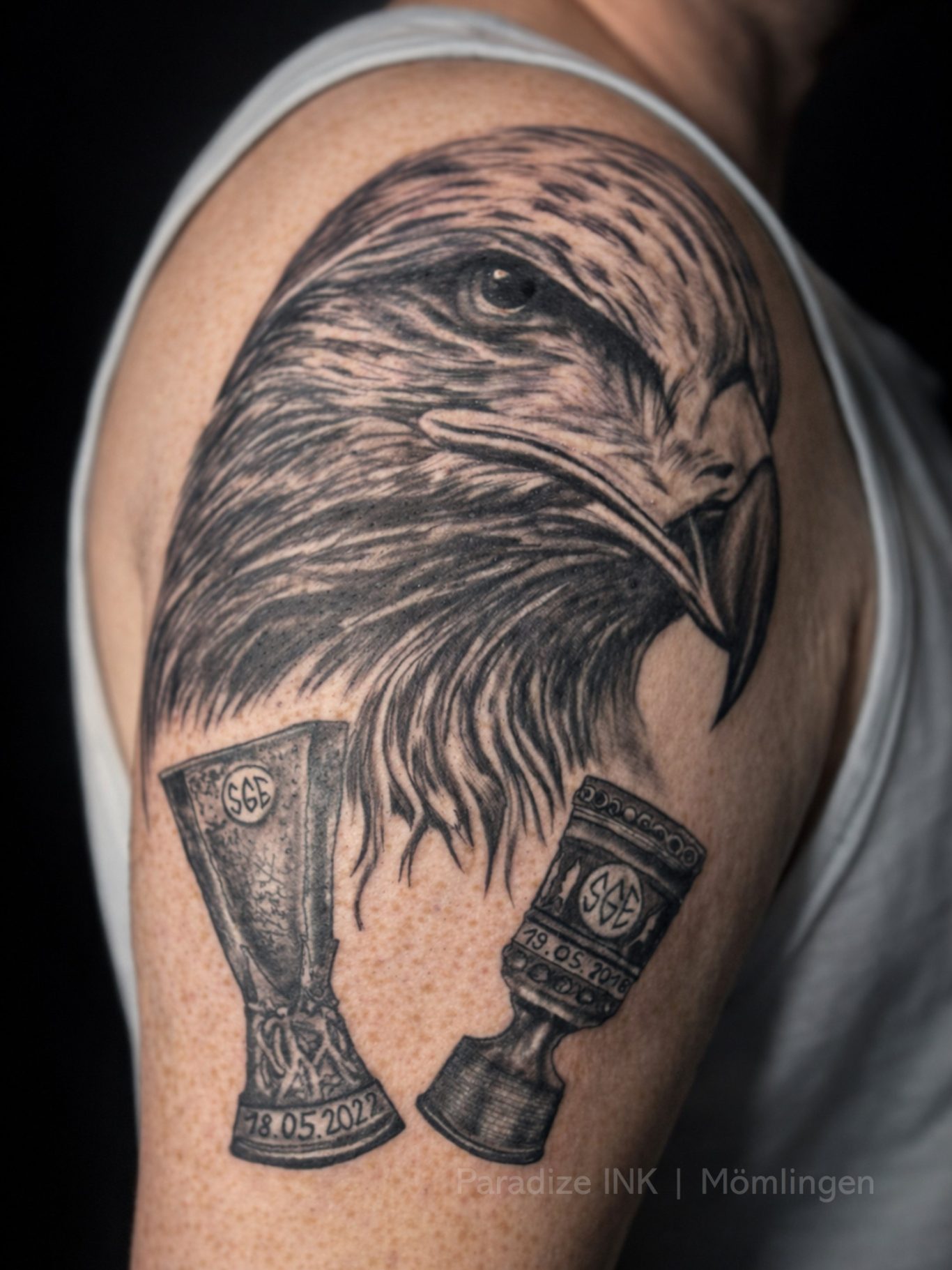 Paradize INK Tattoo Mömlingen Ein tätowierter Adlerkopf neben zwei Pokalen auf dem Oberarm.