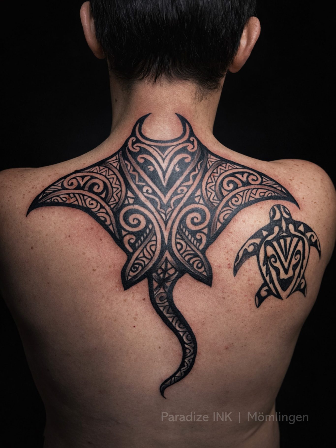 Paradize INK Tattoo Mömlingen Detailreiche Schwarz-Weiß-Tätowierung eines Mantas auf dem Rücken, daneben eine Schildkröte.