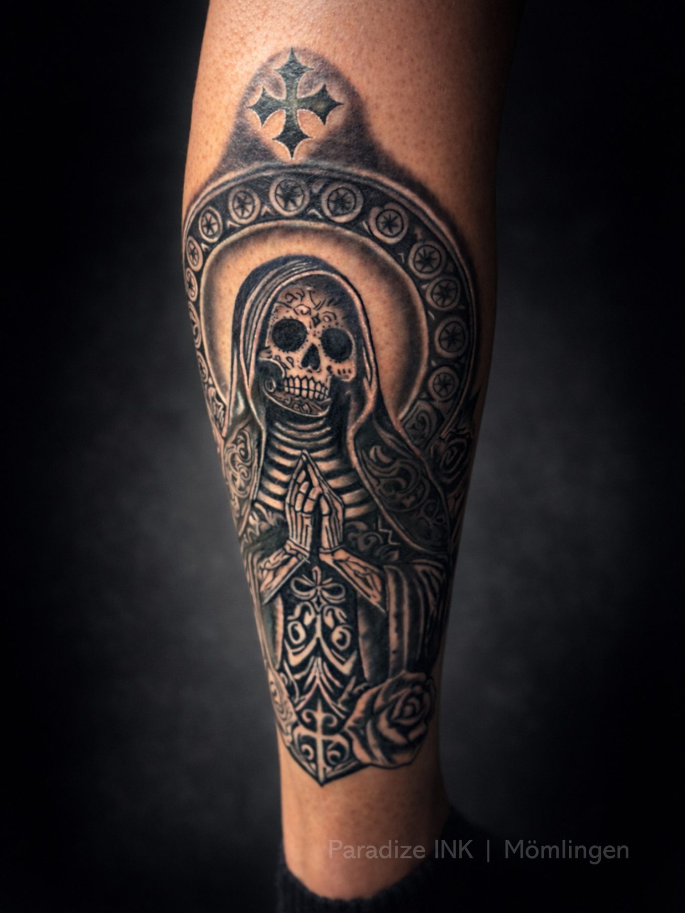 Paradize INK Tattoo Mömlingen Schwarzes Tattoo eines Totenkopfes in der Pose einer betenden Figur mit Ornamenten.