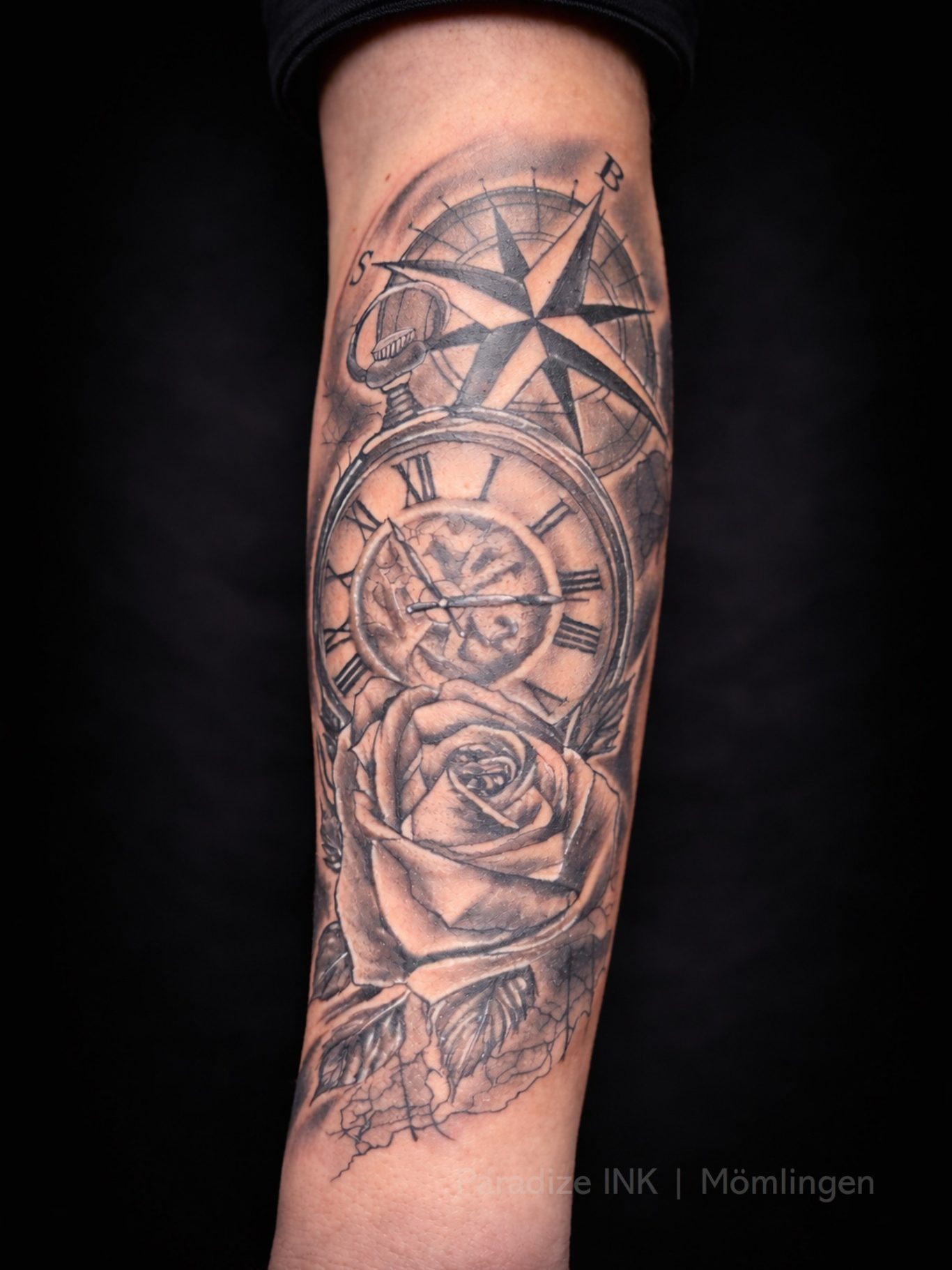 Paradize INK Tattoo Mömlingen Tattoo auf dem Unterarm mit Kompass, Uhr und Rose in Schwarz und Grau.