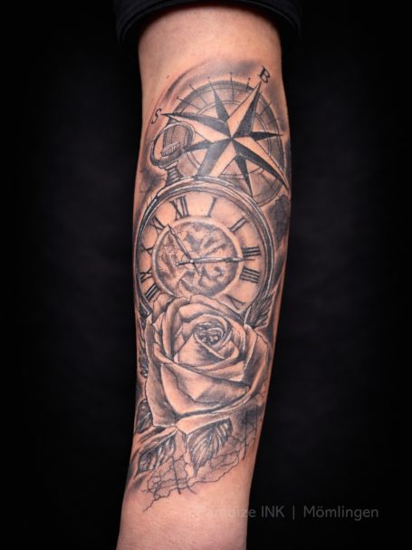 Tattoo auf dem Unterarm mit Kompass, Uhr und Rose in Schwarz und Grau.