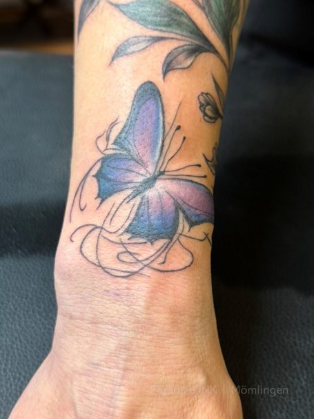 Lila Schmetterling-Tattoo auf dem Handgelenk, umgeben von schwungvollen Linien.