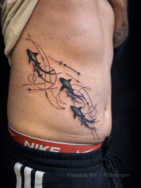 Schwarzes Tattoo mit stilisierten Pfeilen und schwungvollen Linien auf dem Bauch.