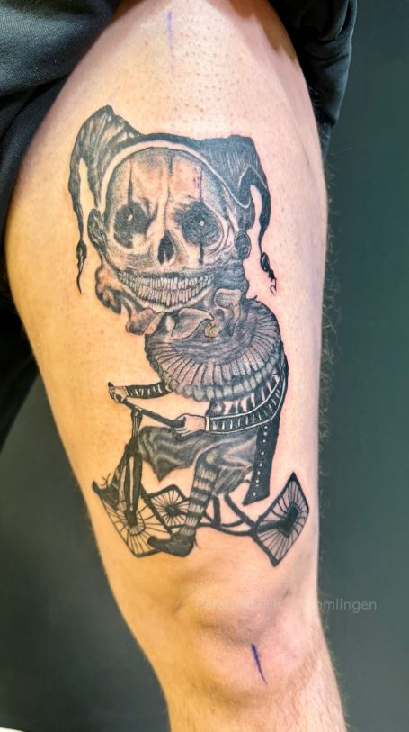 Tattoo eines Schädels, umgeben von verschiedenen Objekten und Details auf einem Oberschenkel.