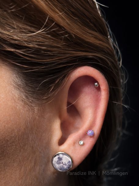 Nahaufnahme eines Ohres mit mehreren Ohrsteckern und einem Helix-Piercing.