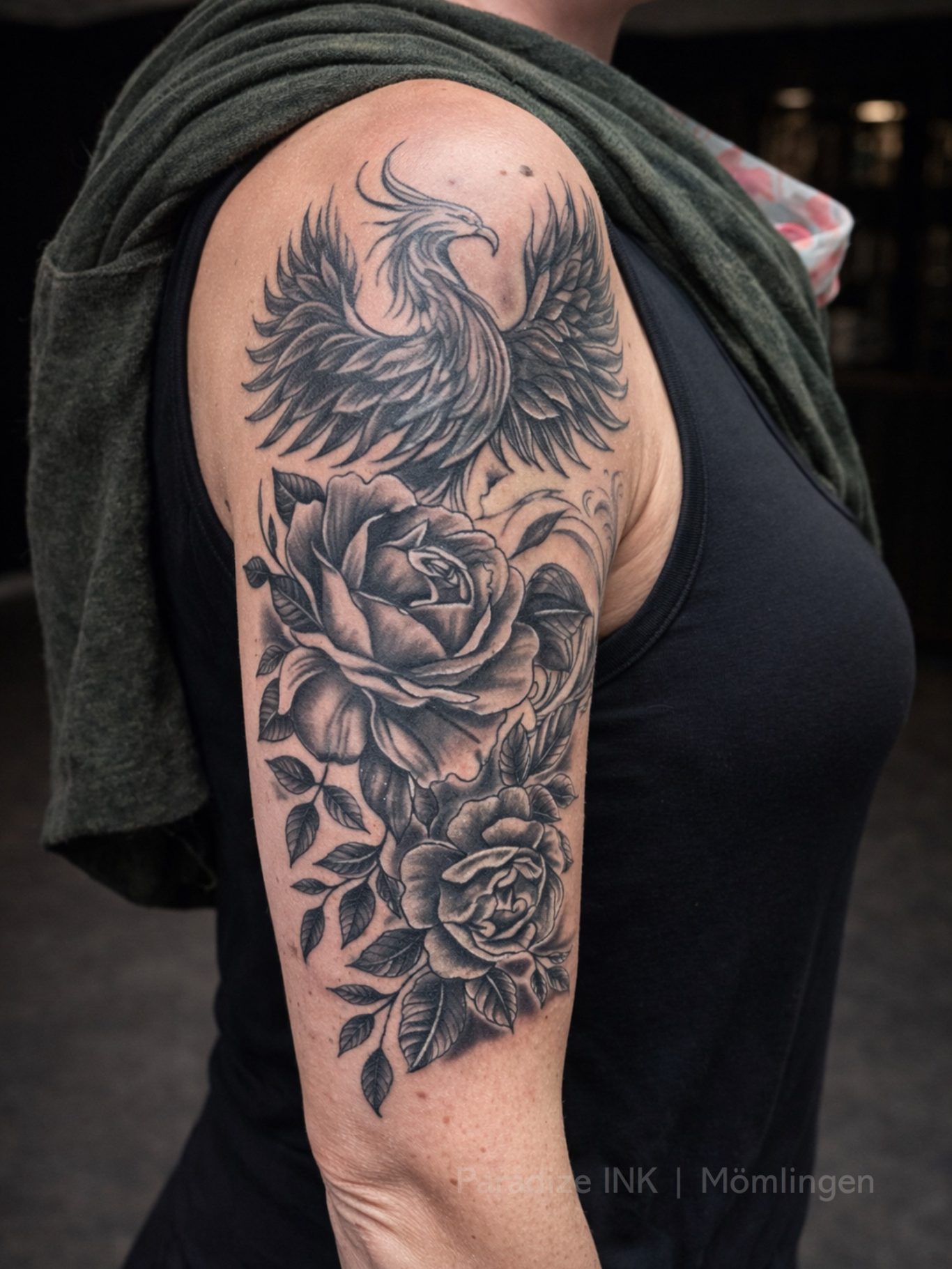 Paradize INK Tattoo Mömlingen Tattoo eines Phönix und Rosen auf dem Oberarm einer Person.