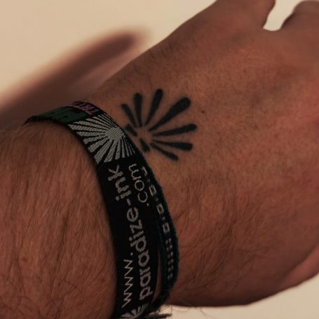 Ein Handgelenk mit einem schwarzen Tattoo und einem bunten Festivalarmband.