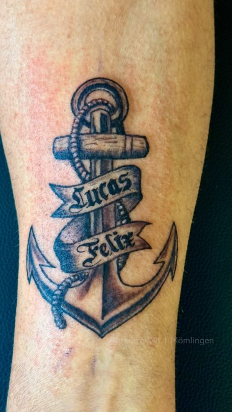 Ein Anker mit einem Banner, auf dem "Lucas" steht, auf einem Unterarm tätowiert.