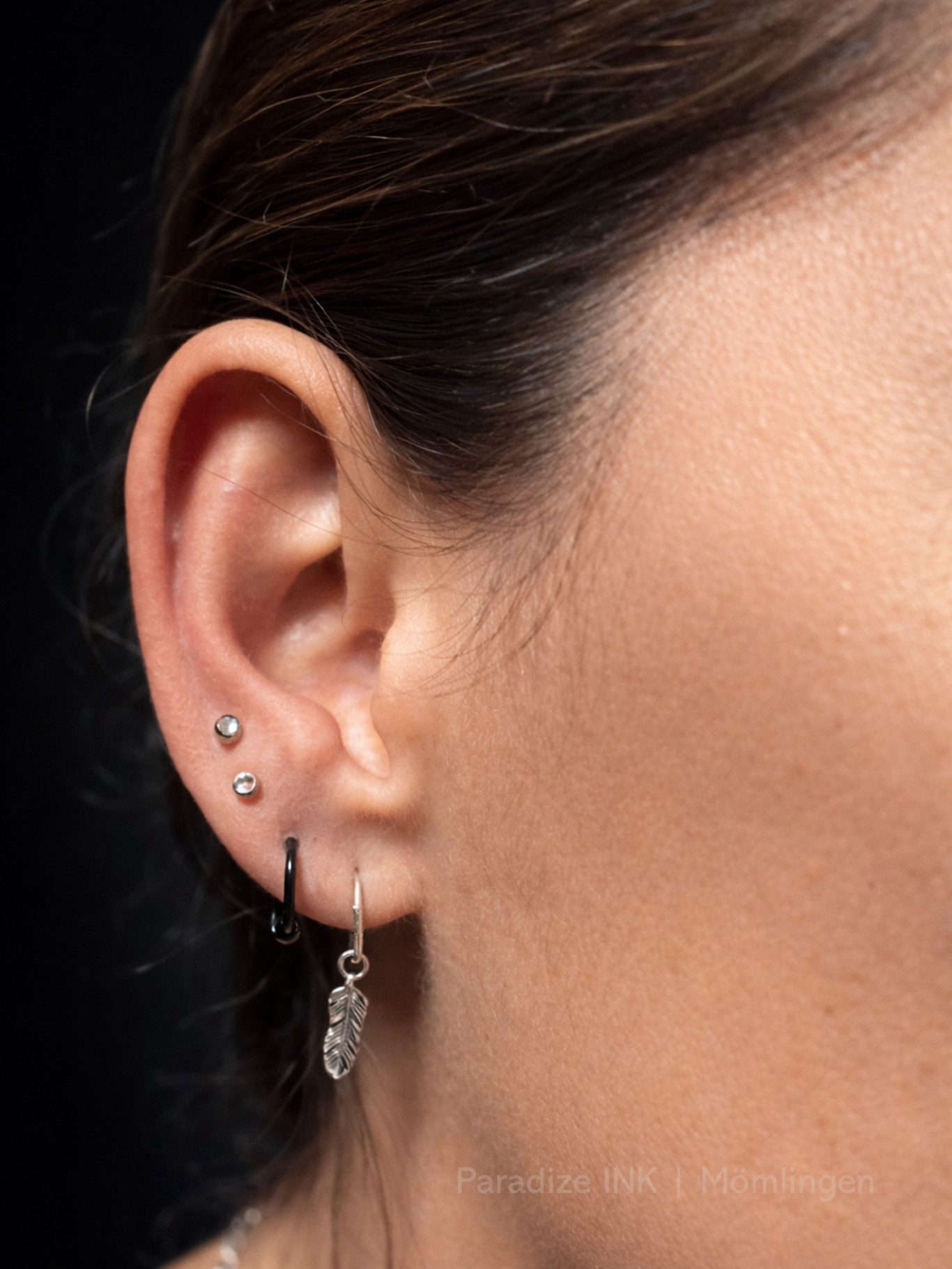Paradize INK Tattoo Mömlingen Nahaufnahme eines Ohrs mit mehreren Ohrlöchern und verschiedenen Ohrringen.