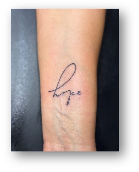 Tattoo auf dem Unterarm mit dem Wort "hope" in geschwungener Schrift.
