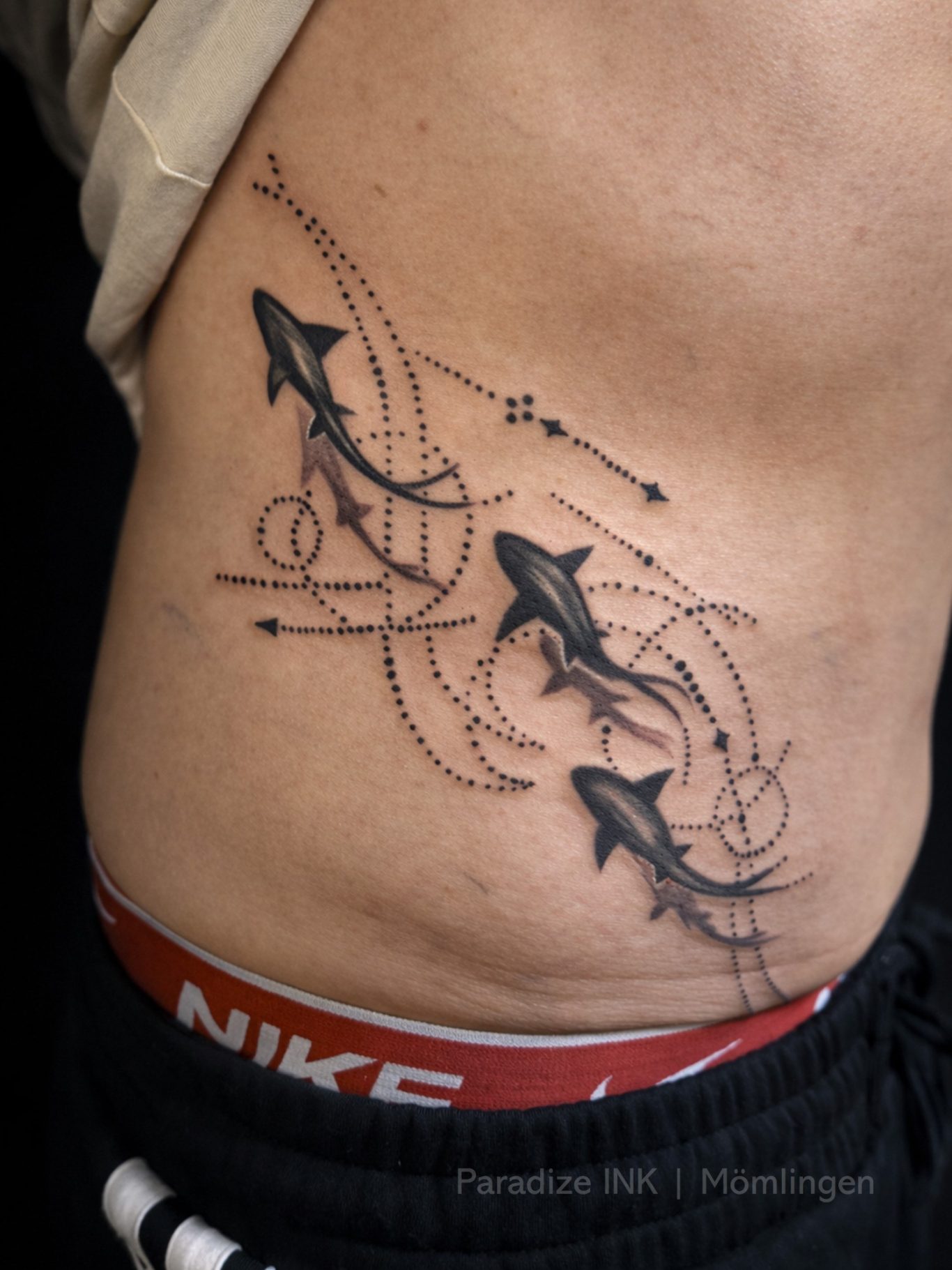 Paradize INK Tattoo Mömlingen Tätowierung mit stilisierten Pfeilen und geschwungenen Linien auf der Seite des Körpers.