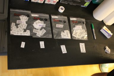 Drei durchsichtige Beutel mit beschrifteten Zetteln auf einem Tisch, daneben ein Marker.