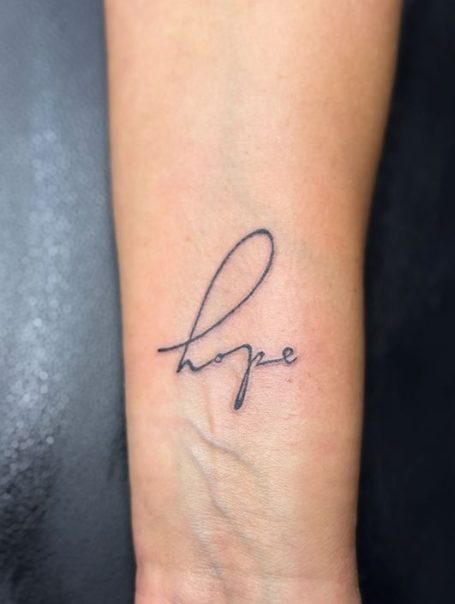 Tätowierung des Wortes "hope" in kursiver Schrift auf dem Handgelenk.