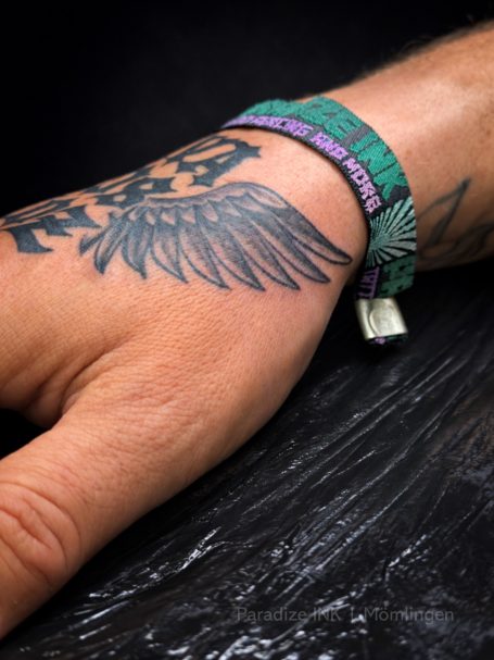 Tattoo eines fliegenden Adlers auf einem Handgelenk mit einem bunten Armband.