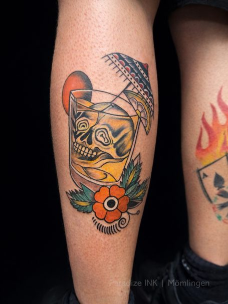 Tattoo eines Schädels in einem Glas mit einer blühenden Blume und einem kleinen Schirm.