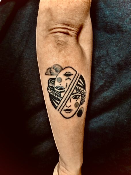 Tattoo auf einem Unterarm mit einem grafischen Design und einer Gesichtsdarstellung.