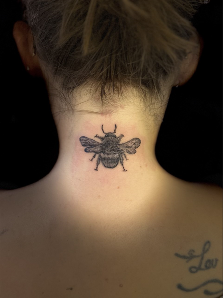 Schwarze Biene als Tattoo am Nacken einer Person.