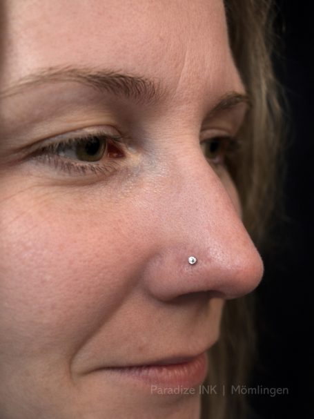Nahaufnahme eines Gesichts mit Nasenpiercing und sanftem Lächeln.