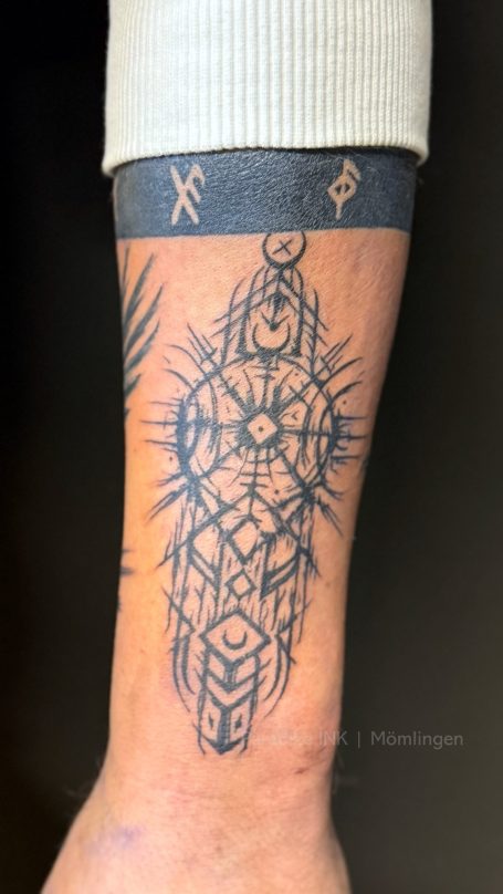 Tattoo auf dem Unterarm mit geometrischen Mustern und strahlenförmigen Elementen.